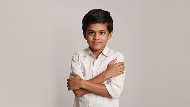 Confident young boy standing with crossed arms wearing light buttoned shirt portrait