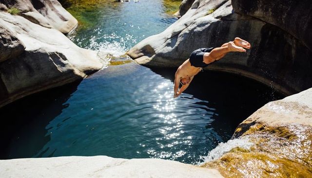 Diving man launching into sunlit granite plunge pool at remote canyon