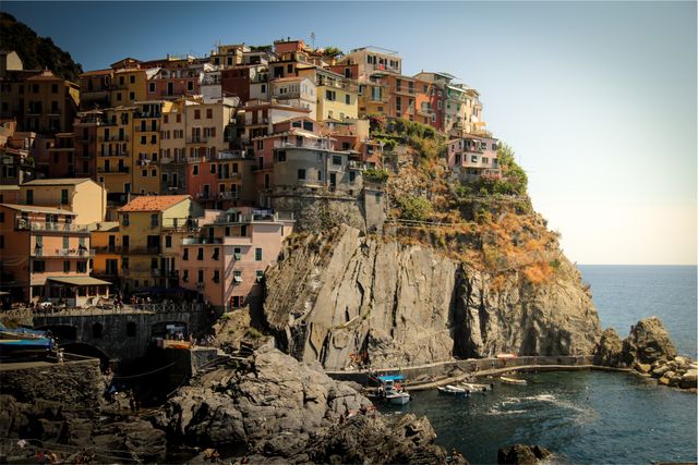 Colorful buildings of Italian Riviera village perched on rocky cliff by Mediterranean Sea. Ideal for promoting travel, tourism, and architecture of coastal towns in Italy. Suitable for travel blogs, brochures, and posters highlighting scenic European destinations.