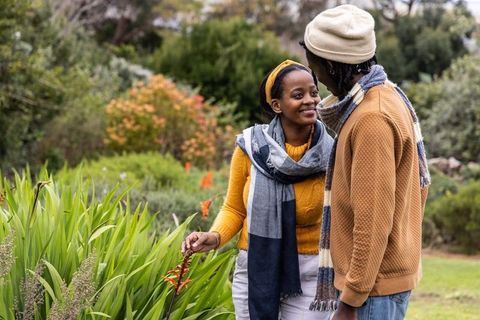 African american couple admiring orange bloom in garden wearing cozy autumn scarves