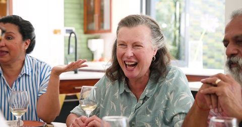 Senior Friends Enjoying Wine and Laughing Together at Dinner Table