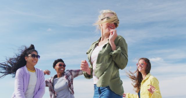 Group of diverse friends enjoying sunny day outdoors, smiling and laughing together. Women wearing casual clothes and exuding a cheerful mood. Perfect for themes of friendship, leisure activities, summer joy, and social connections.