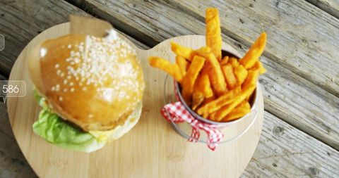 Gourmet burger with sesame bun and sweet potato fries on wooden board for outdoor picnic