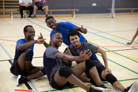 African american volleyball teammates taking selfie while relaxing on indoor court