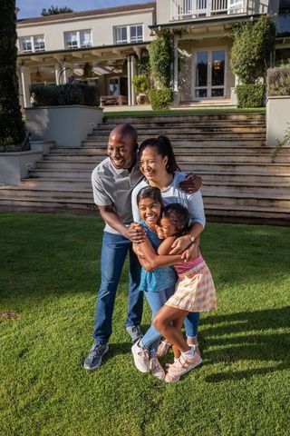 Happy Family Embracing on Green Lawn in Front of House