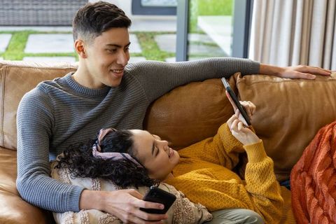 Couple relaxing on leather sofa scrolling smartphones, cozy home lounge romance