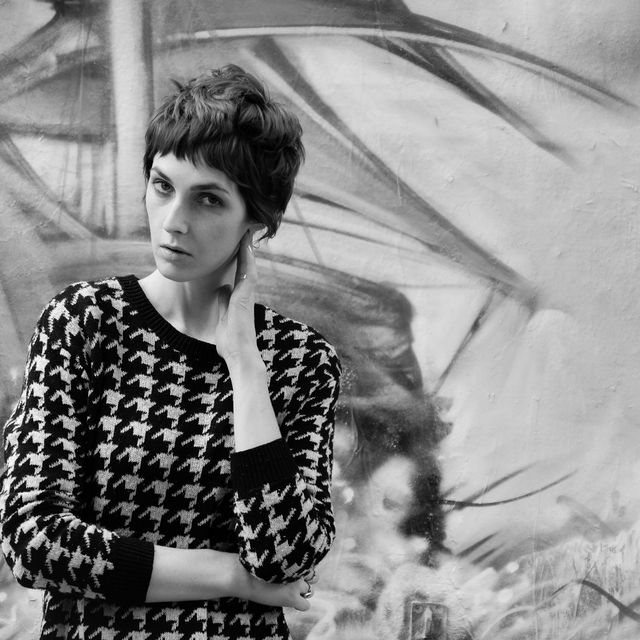 Monochrome portrait featuring a Caucasian woman wearing a stylish sweater, posing pensively against a graffiti mural. Ideal for fashion editorials, urban art campaigns, and artistic photography collections highlighting style and modern trends.