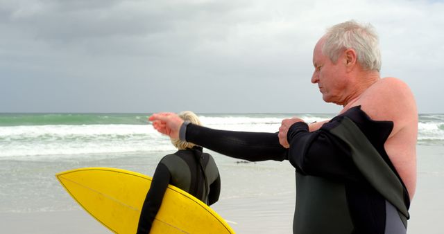 Senior Surfer Putting on Wetsuit at Beach with Yellow Surfboard - Download Free Stock Images Pikwizard.com