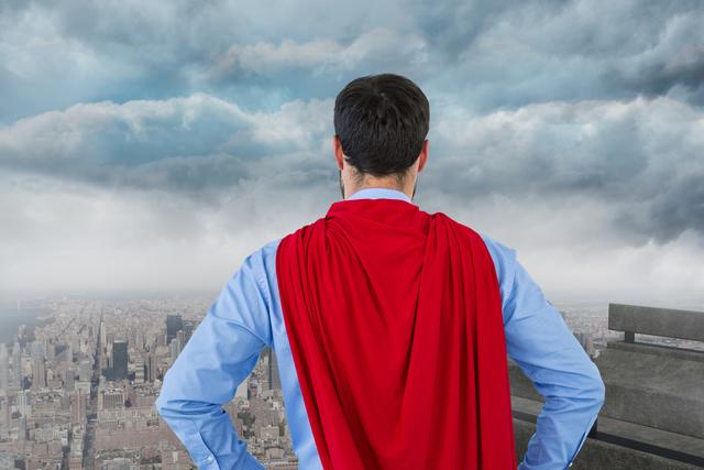 Back view of a businessman in a super hero cape standing on a rooftop overlooking the city. This can be used to illustrate themes of confidence, leadership, ambition, and professional strength. Ideal for business, motivational, and inspirational contexts.
