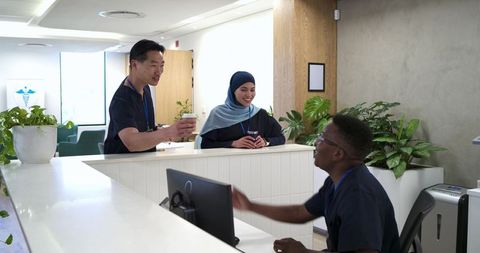 Diverse medical team chatting at modern clinic reception desk with plants and coffee
