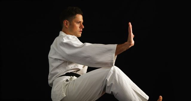 Karate master in white uniform with black belt demonstrates precise palm strike technique in focused stance. Useful for martial arts training programs, self-defense tutorials, sports advertisements, and motivational posters.