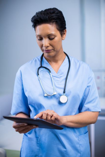 Female nurse in blue uniform using digital tablet in hospital ward. Ideal for healthcare technology, medical staff, patient care, and modern healthcare themes.