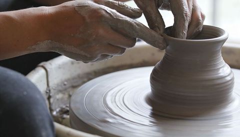 Clay hands shaping vase on pottery wheel closeup of potter pinching and smoothing rim