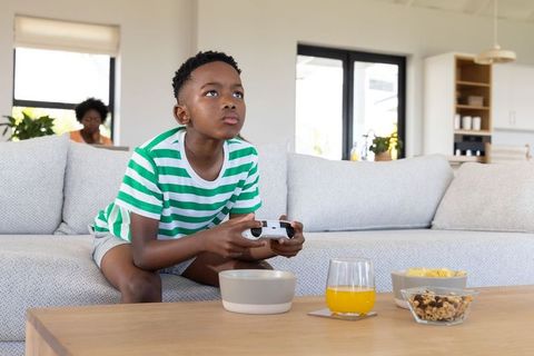 African american boy playing video games on couch in sunlit modern open-plan living room