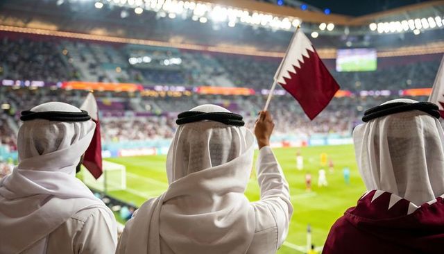 Qatari supporters waving flag in stadium wearing kandura and ghutra during night match