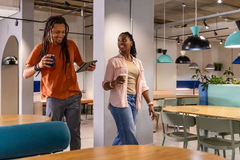 African american coworkers walking and chatting in modern coworking lounge with coffee and tablet