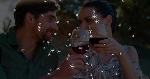Couple toasting red wine at dusk in outdoor garden with sparkling star bokeh