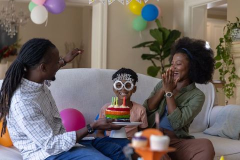 Black family celebrating birthday at home with rainbow layer cake and party balloons