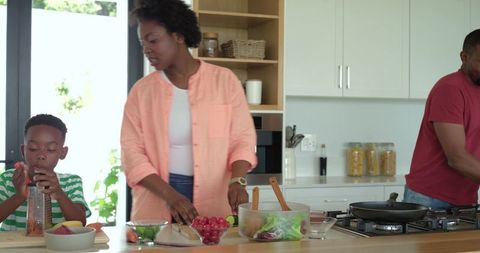African american family preparing meal in sunlit kitchen, child grinding spices