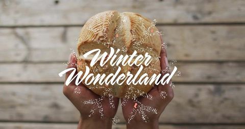 Hands holding rustic scored loaf with winter wonderland script and festive gold glitter