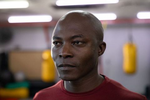 Serious african american boxer standing in gym near yellow punching bag, athletic portrait