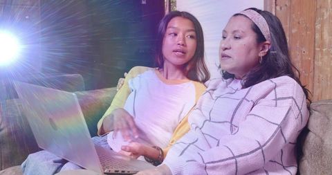 Multigenerational asian women sharing laptop on cozy sofa discussing online content