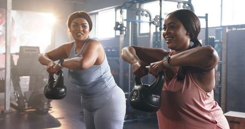 Friends lifting kettlebells during energetic gym workout with fitness watches