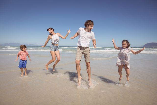Cheerful family jumping on shore at beach against clear blue sky