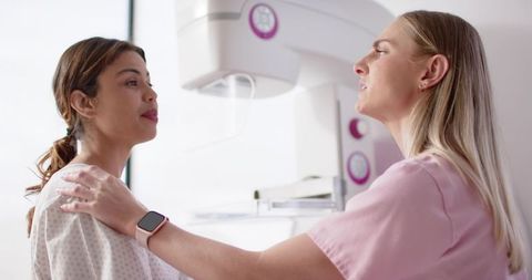 African American woman receiving mammogram as radiology technician positioning paddle