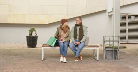 Mature couple laughing on city bench after shopping, casual fall outfits, relaxed weekend