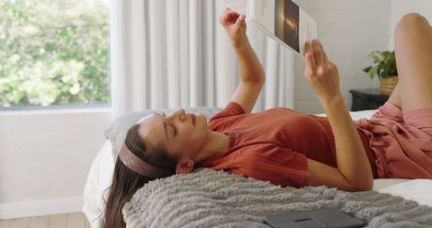 Woman relaxing on bed reading book in cozy home