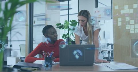 Female colleagues collaborating on laptop and strategy documents in modern glass office