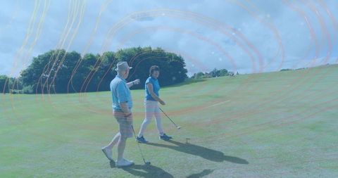 Senior couple walking on sunny golf course wearing blue polos carrying clubs and tee ball
