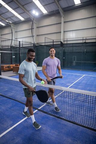 Friends playing indoor paddle sport on blue court, serving ball at net