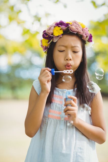 Girl wearing flower wreath blowing bubble wand in park