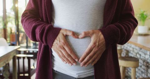 Pregnant Woman Forming Heart Over Belly Indoors