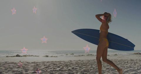 Surfer woman walking with blue surfboard on sunny beach