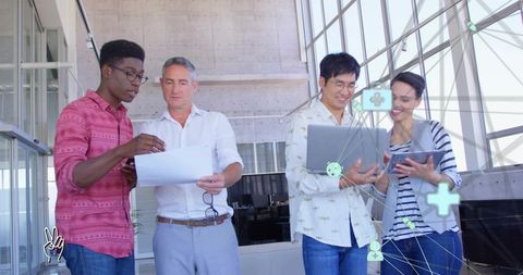 Multicultural team collaborating in modern office atrium reviewing documents and devices