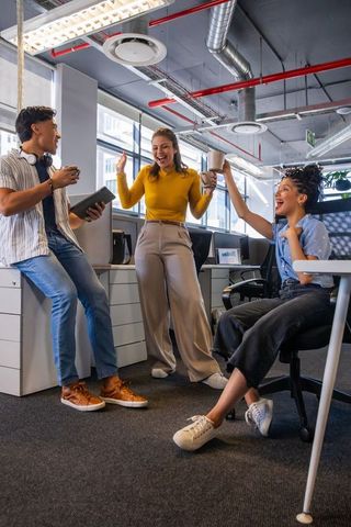 Diverse team celebrating success, collaborating and sharing coffee in modern open-plan office