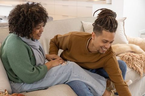 Young couple relaxing on couch, man reaching for phone, cozy modern living room moment