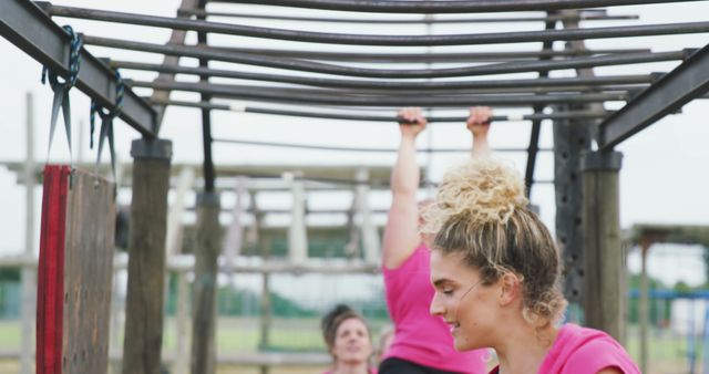 Caucasian women in pink t shirts at the monkey bars on bootcamp training course. Female fitness, friendship, challenge and healthy lifestyle.