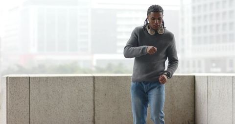 Checking smartwatch on rooftop while walking wearing headphones and casual sweater