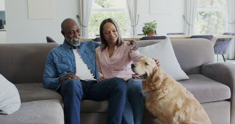 Mature couple relaxing on sofa petting golden retriever in bright cozy living room