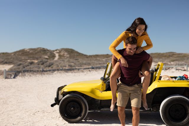 Happy caucasian couple piggybacking from beach buggy on sunny beach. beach stop off on romantic summer holiday road trip.