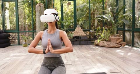 Woman Practicing Yoga with VR Headset in Serene Glass House