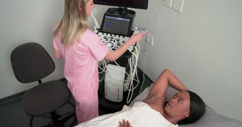 Sonographer performing diagnostic breast ultrasound on african american woman in clinic