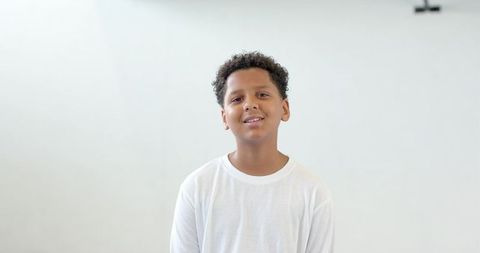 Contemplative young boy standing against pale wall indoors