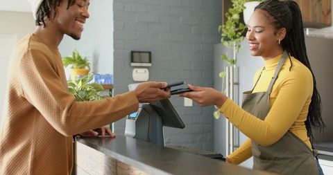 Customer tapping phone for contactless payment while cashier smiling at cafe counter