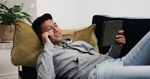 Young Man Relaxing on Sofa Using Smartphone and Tablet at Home