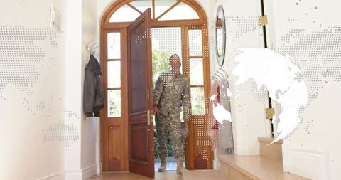 Soldier returning home entering sunlit foyer holding helmet in camouflage uniform welcoming moment